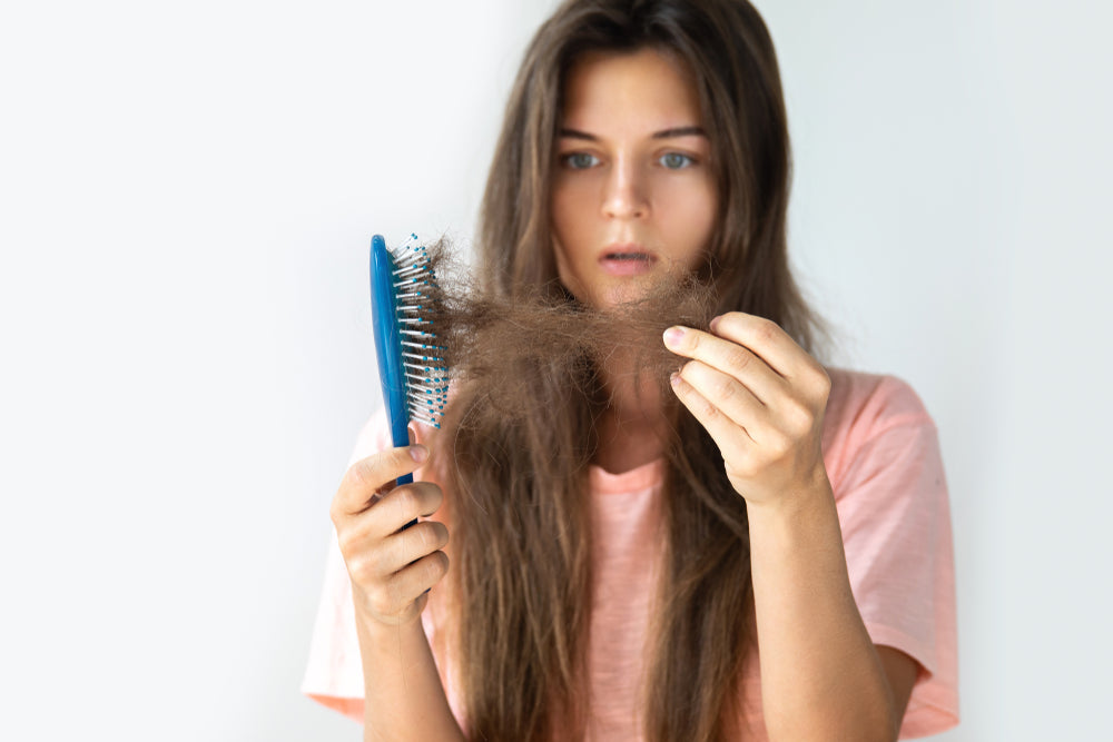 woman with shocked expression looking at a hairbrush full of her hair