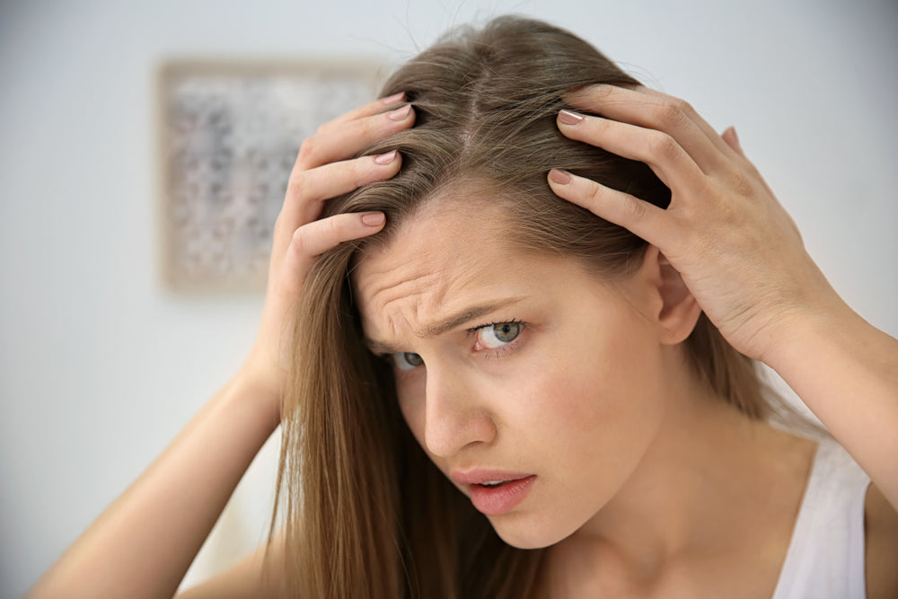 Woman examining her scalp and hairline in a mirror while wondering why does my scalp hurt