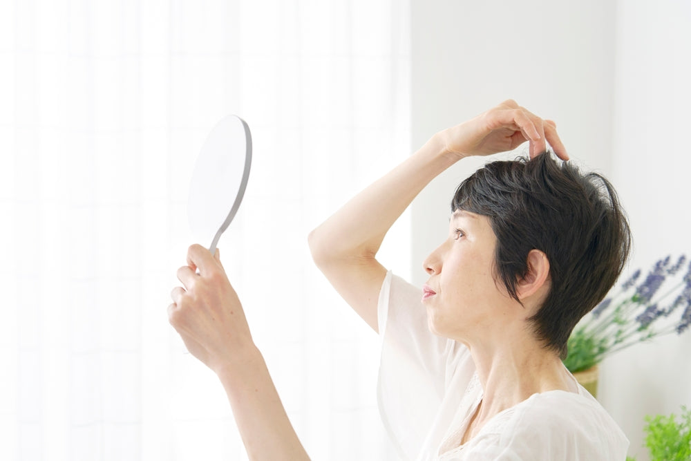 Woman checking her scalp in a mirror after noticing signs that may explain why her hair is thinning.